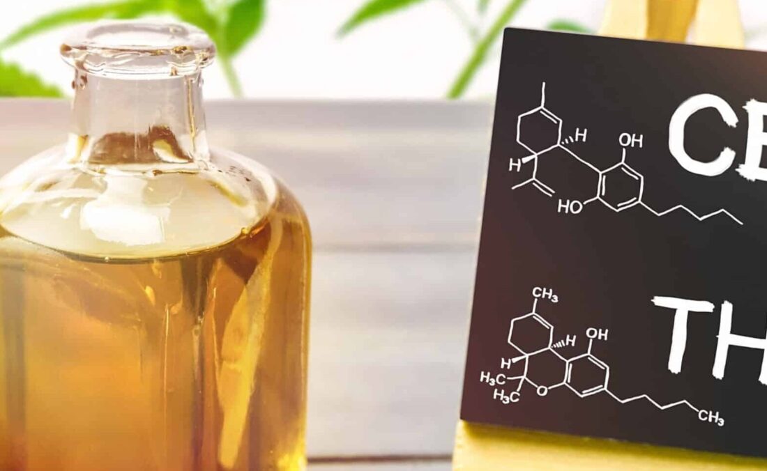 A bottle of canabis oil sits next to a miniature black board that reads CBD and THC while showing the molecule models